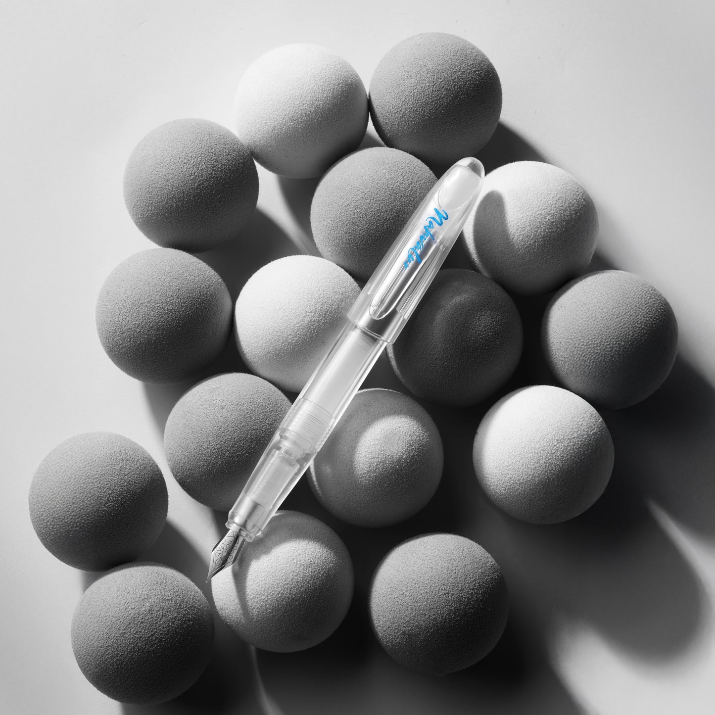 Clear pen lying on gray spherical objects with a light gray background