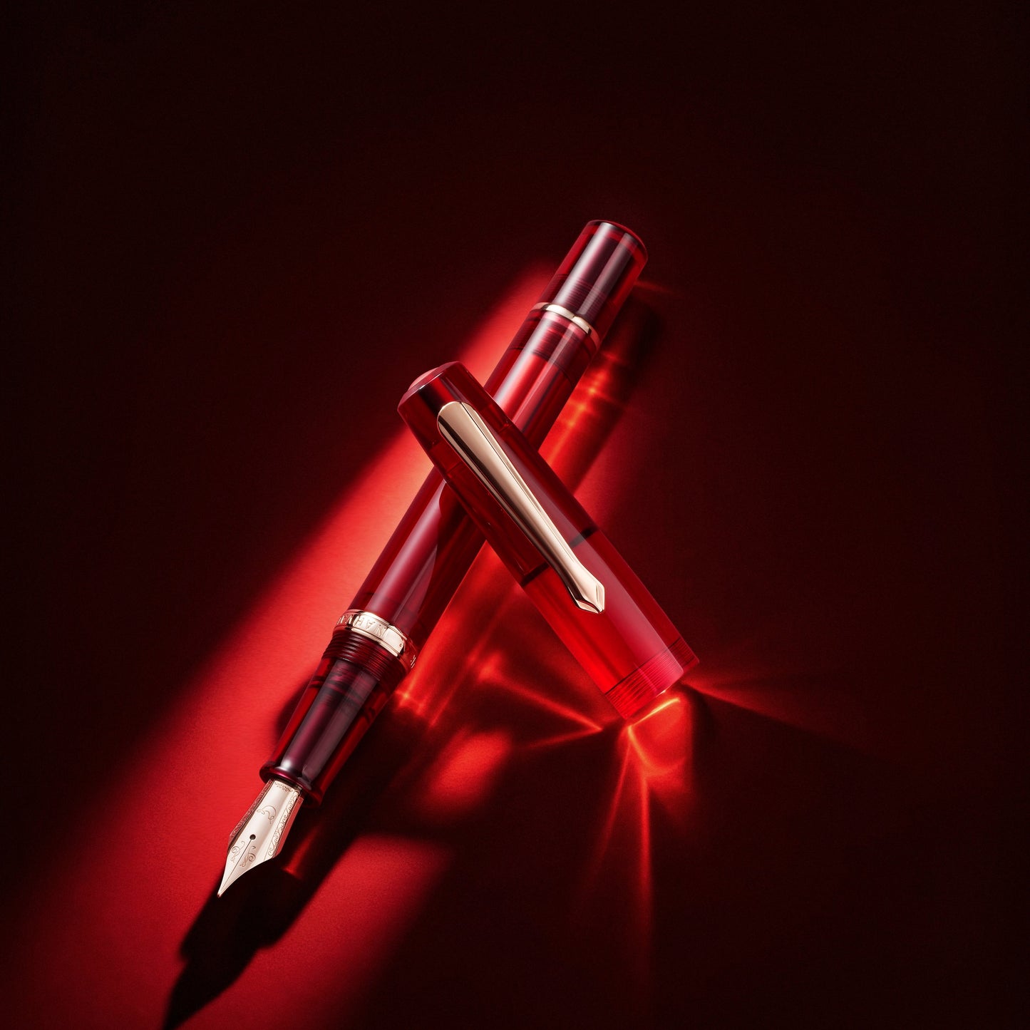 
                  
                    A luxury fountain pen with a glossy red translucent barrel and gold-toned trim, positioned diagonally on a dark red background with dramatic spotlighting and reflections.
                  
                