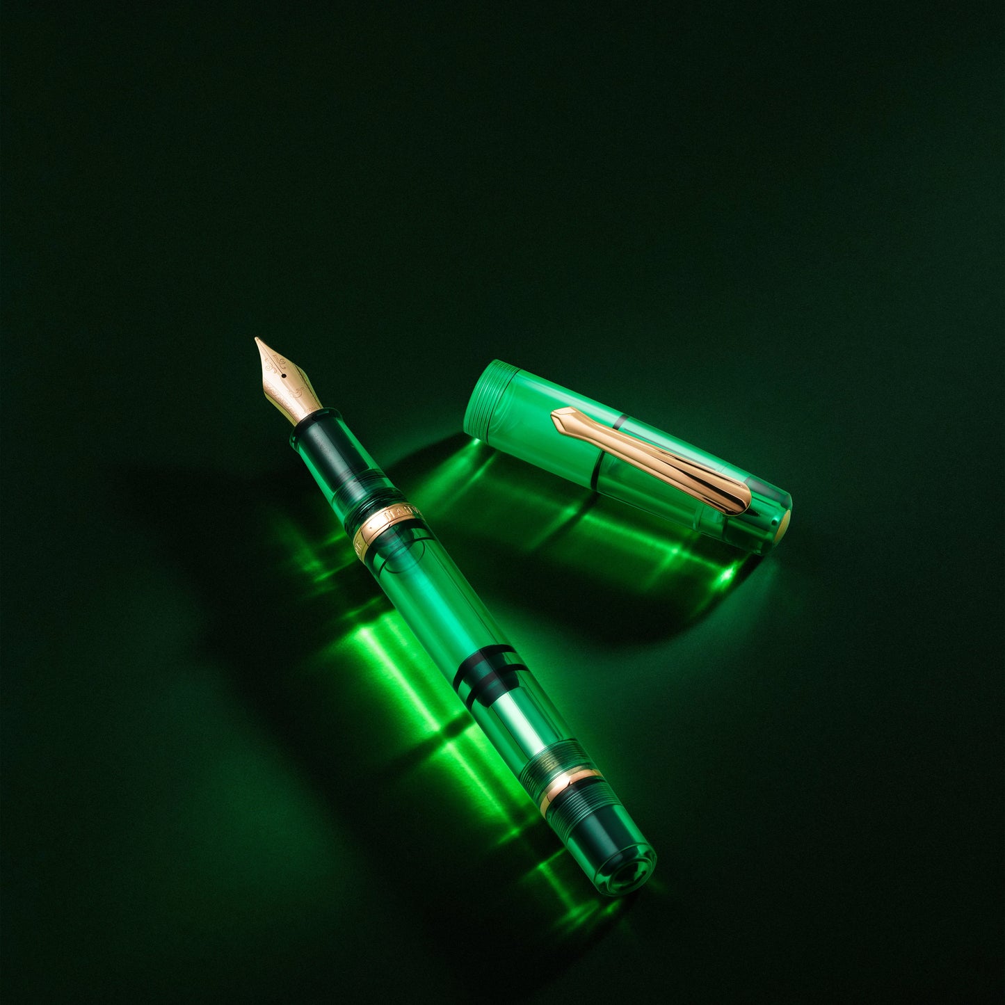 
                  
                    A green transparent fountain pen with a gold nib and trim, shown with its cap off on a dark black background.
                  
                