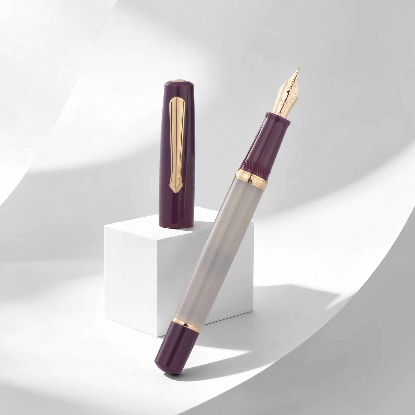 
                  
                    A luxury fountain pen with a translucent gray barrel and deep purple accents, shown with its cap off on a white pedestal against a modern white background with soft shadows.
                  
                