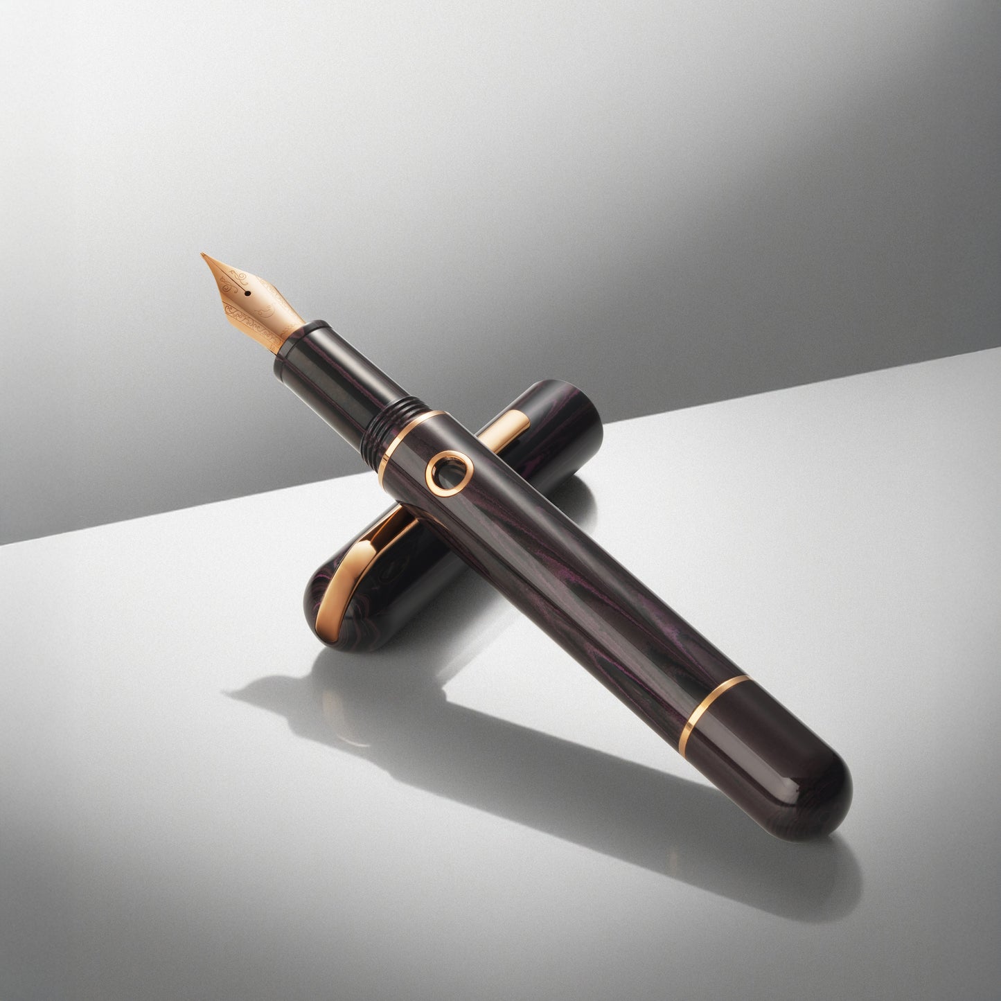Fountain pen with a dark berry body and rose gold accents on a reflective surface.
